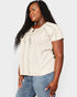 Woman wearing a beige blouse with lace details and blue jeans on a light gray background