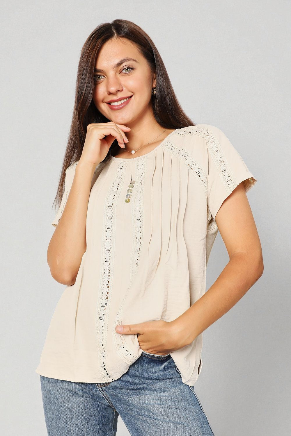 Woman wearing a beige top with lace details and blue jeans on a gray background