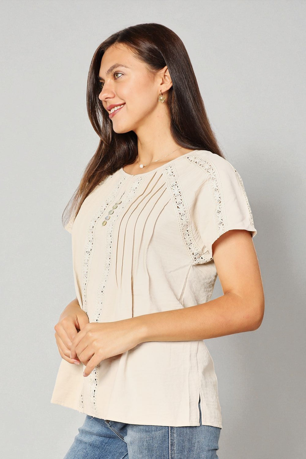 Woman wearing a beige blouse with lace details on a gray background