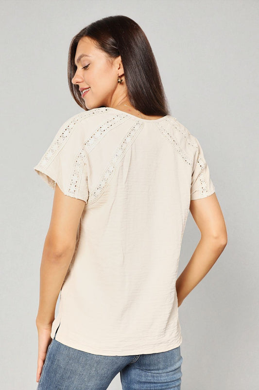Woman wearing a beige short-sleeve top with lace details on a gray background