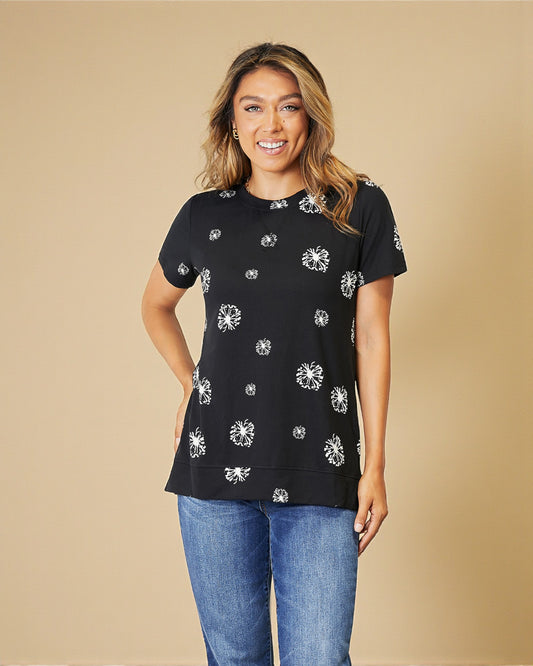 Woman wearing a black t-shirt with white floral patterns and blue jeans on a beige background