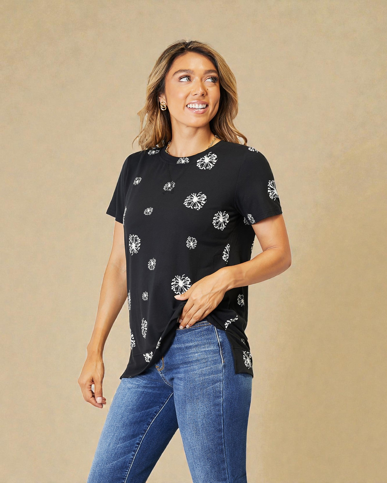 Woman wearing a black t-shirt with white patterns and blue jeans on a beige background