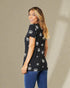 Woman wearing a black floral-patterned top and blue jeans against a beige background