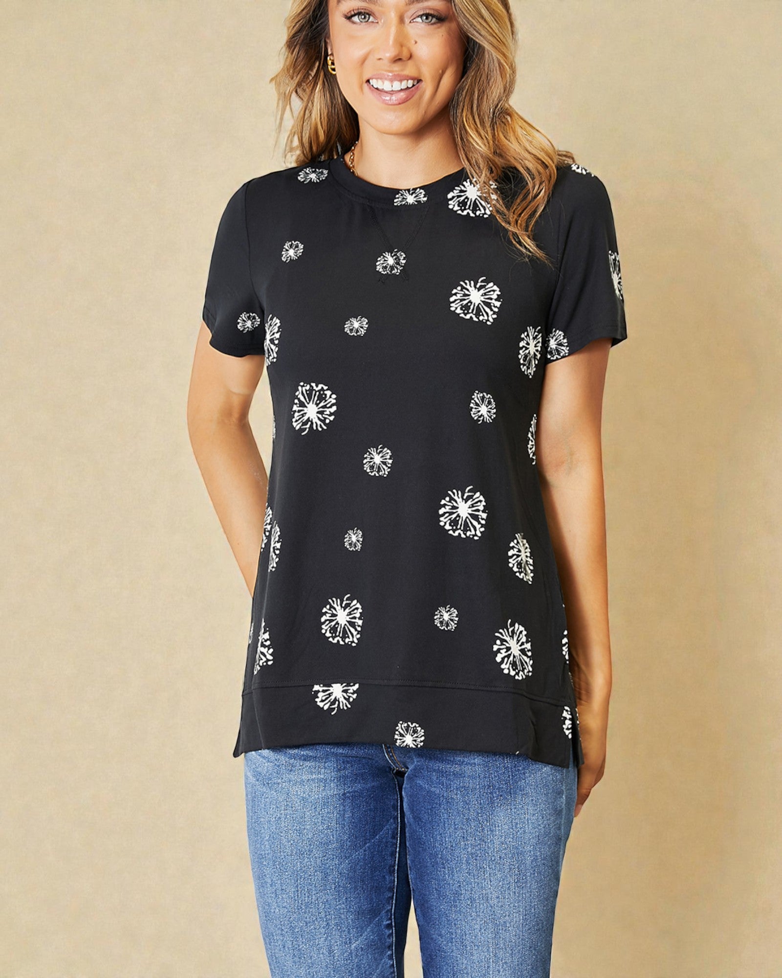 Woman wearing a black top with white floral patterns and blue jeans on a beige background