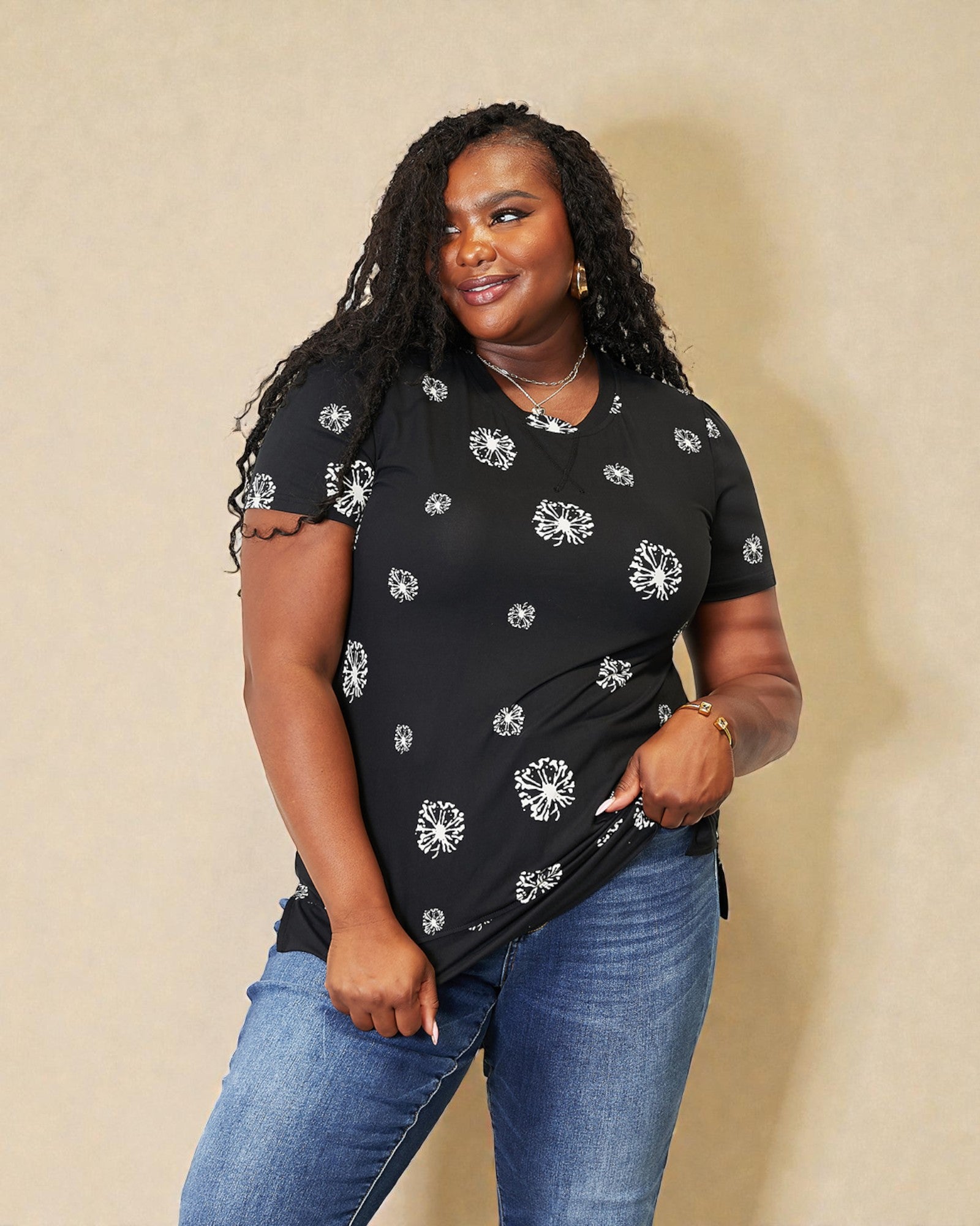Woman wearing a black t-shirt with white floral patterns and blue jeans against a beige background