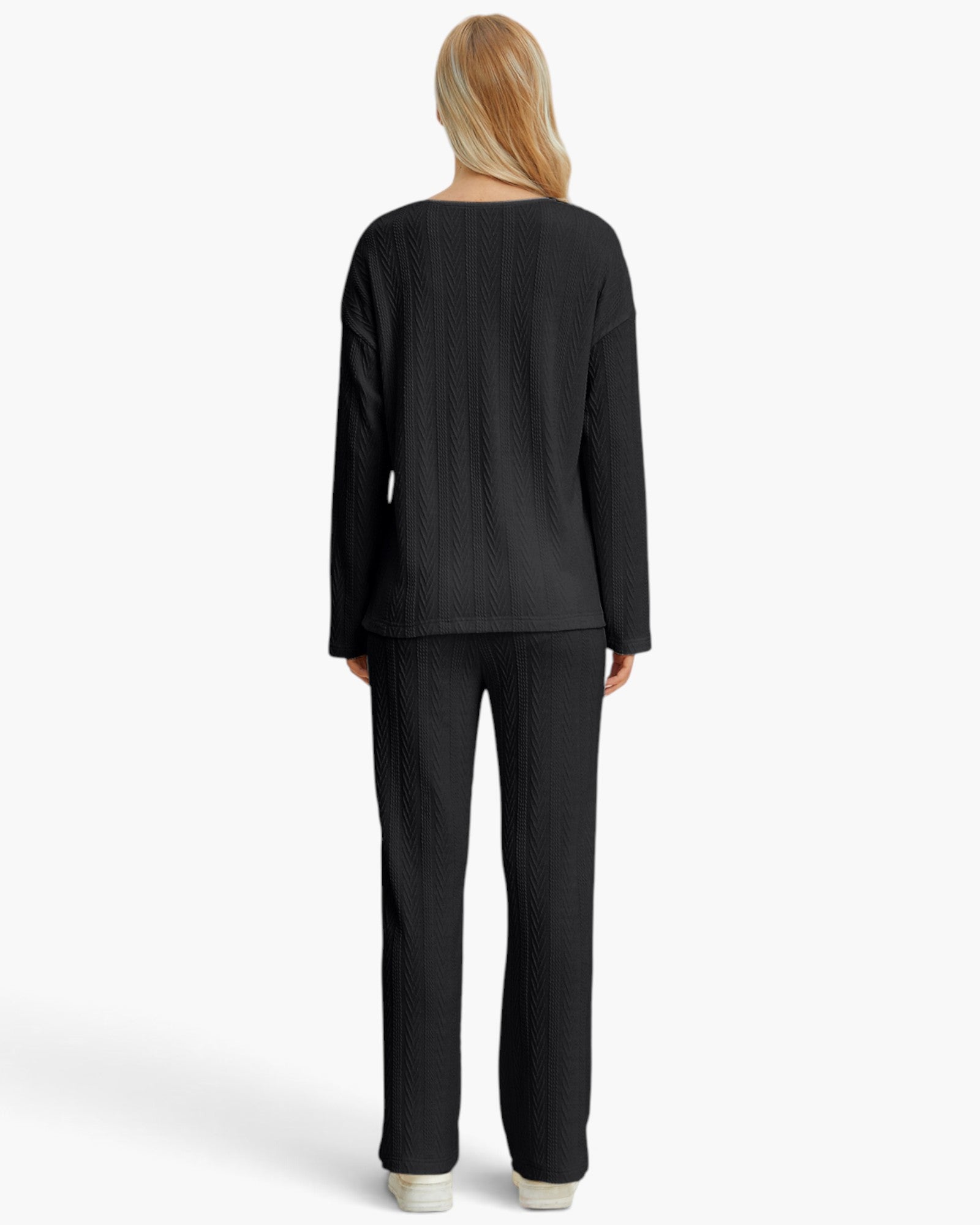 A woman viewed from the back wearing a matching black textured knit top and wide-leg pants, standing against a plain light gray studio background.