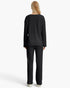 A woman viewed from the back wearing a matching black textured knit top and wide-leg pants, standing against a plain light gray studio background.