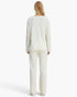 A woman viewed from the back wearing a cream-colored ribbed knit lounge set consisting of a long-sleeve top and matching wide-leg pants, set against a plain white studio background.