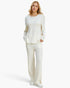 A woman modeling a matching cream-colored knit lounge set consisting of a long-sleeve henley top and wide-leg trousers, paired with white sneakers against a plain white studio background.