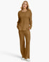 A woman modeling a matching two-piece knit lounge set in a warm camel brown color, featuring a long-sleeve top with a split neckline and wide-leg pants, against a plain white studio background.