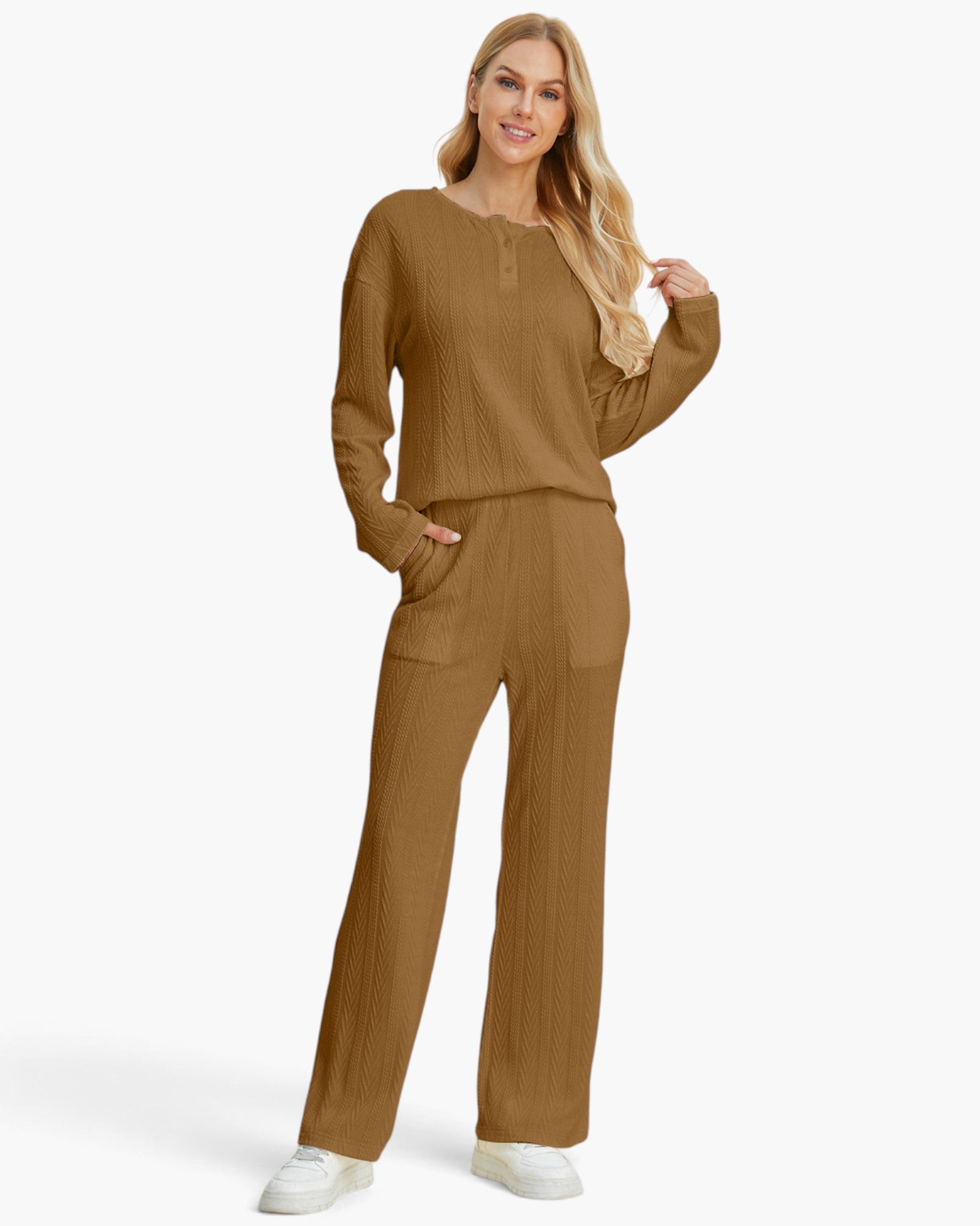 A woman modeling a matching two-piece knit set consisting of a long-sleeve henley top and wide-leg pants in a warm camel brown color, paired with white sneakers against a plain white studio background.