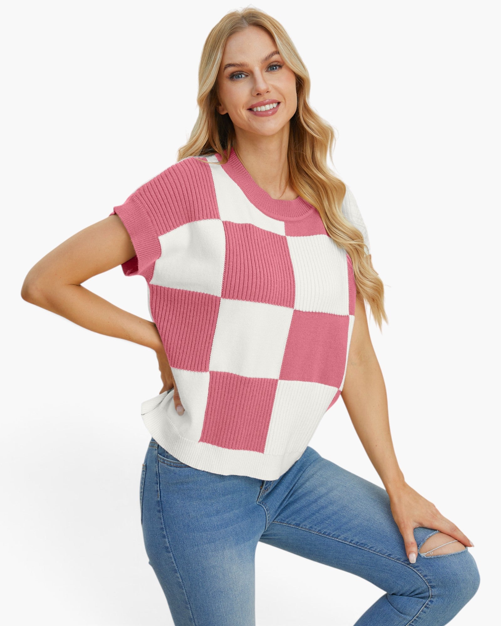 A woman modeling a short-sleeve knit sweater with a pink and white checkerboard pattern, paired with blue jeans, against a plain white background.