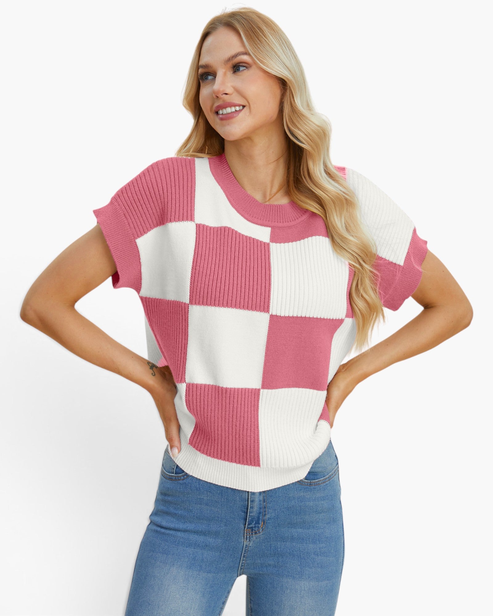 A woman modeling a short-sleeve knit top with a pink and off-white checkerboard pattern, paired with blue jeans, against a plain white studio background.