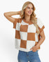 A woman wearing a short-sleeve knit top with a brown and white checkerboard pattern, paired with blue jeans, against a plain white background.
