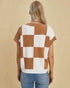 Person wearing a checkered brown and white top with blue jeans on a beige background