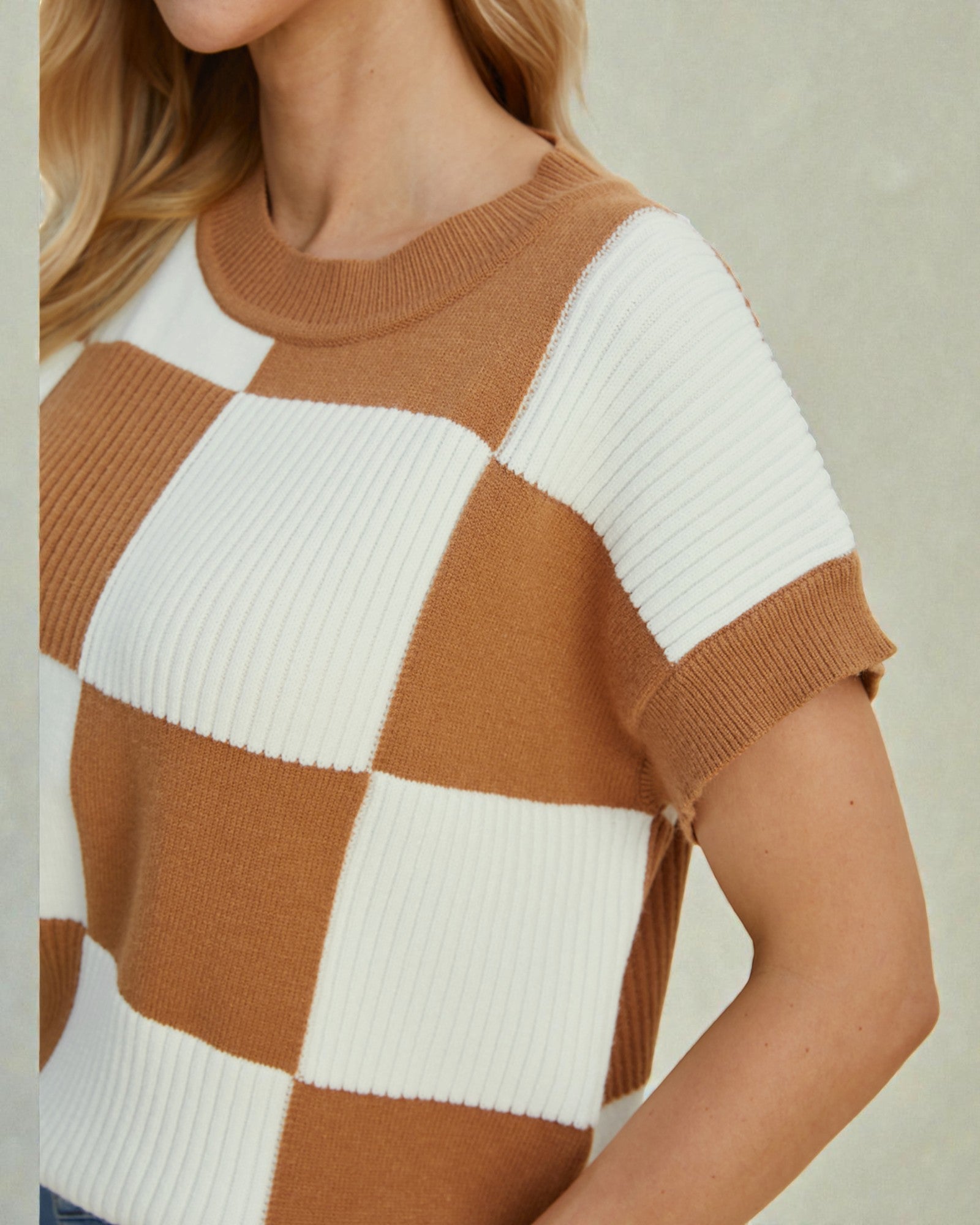 Person wearing a checkered sweater with brown and white squares.