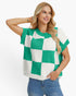 A woman wearing a green and white checkered short-sleeve knit top with textured vertical ribbing, paired with blue jeans, against a plain white background.