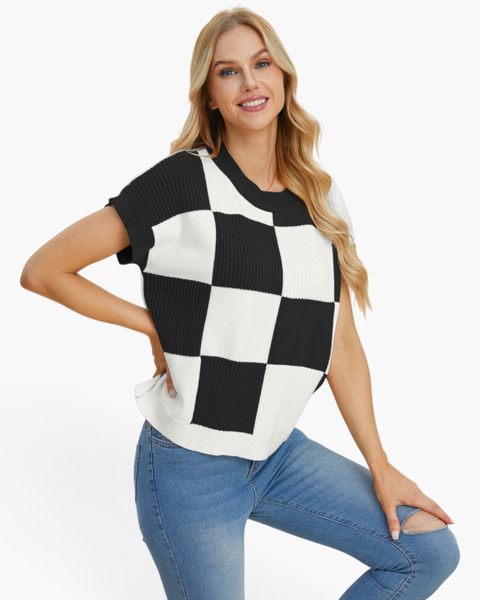 A woman modeling a short-sleeve knit top with a bold black and white checkerboard pattern, paired with blue jeans, against a plain white studio background.