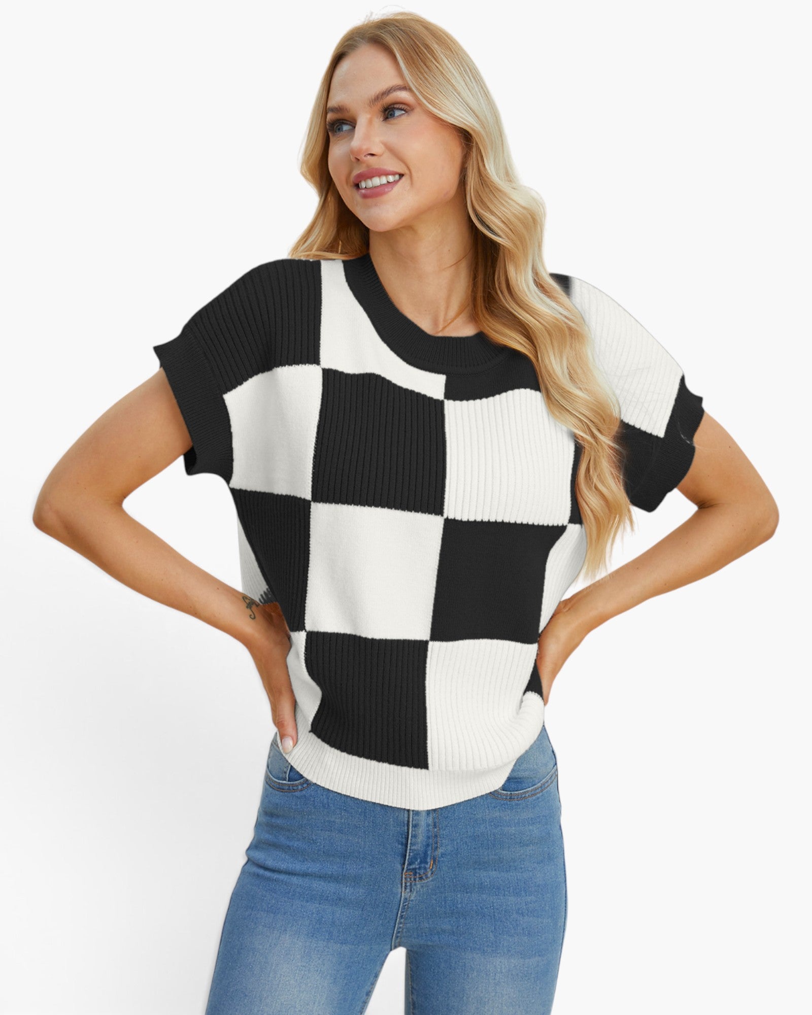 A woman modeling a short-sleeve knit top with a bold black and white checkerboard pattern, paired with blue jeans, against a plain white studio background.