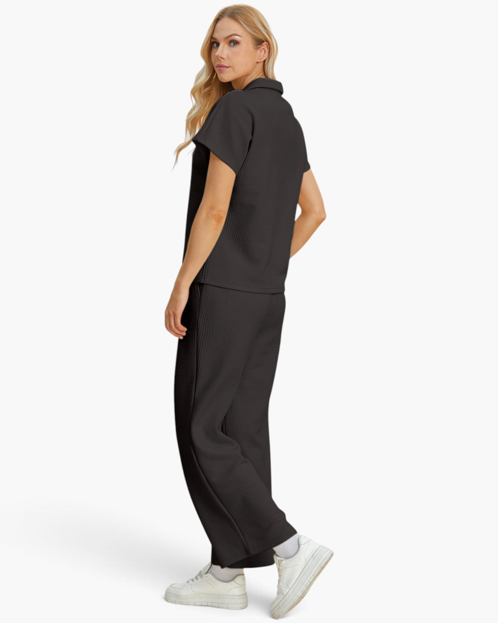 A woman modeling a dark gray short-sleeve scrub top and matching wide-leg scrub pants, shown from a side-back angle against a clean white studio background.
