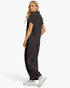 A woman modeling a dark gray short-sleeve scrub top and matching wide-leg scrub pants, shown from a side-back angle against a clean white studio background.
