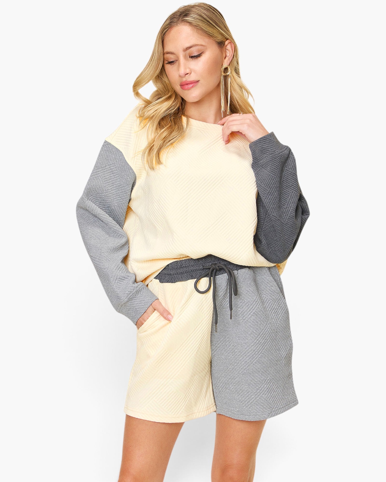 A woman modeling a color-blocked knit lounge set featuring a cream and gray long-sleeve top with matching shorts, set against a plain light gray background.