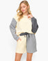A woman modeling a color-blocked knit lounge set featuring a cream and gray long-sleeve top with matching shorts, set against a plain light gray background.