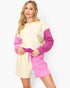 A woman modeling a color-blocked knit romper with a cream body and sleeves, and bright pink shorts and side panels, featuring a matching pink drawstring belt.