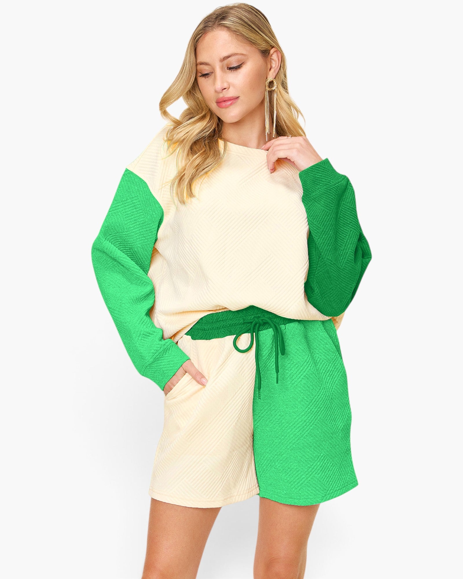 A woman modeling a color-blocked knit romper with a cream body, bright green sleeves, and a matching green drawstring waist, set against a plain light gray studio background.