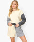 A woman modeling a color-blocked knit jumpsuit with a cream body, gray sleeves, and gray shorts, featuring a matching gray drawstring belt, against a plain white studio background.