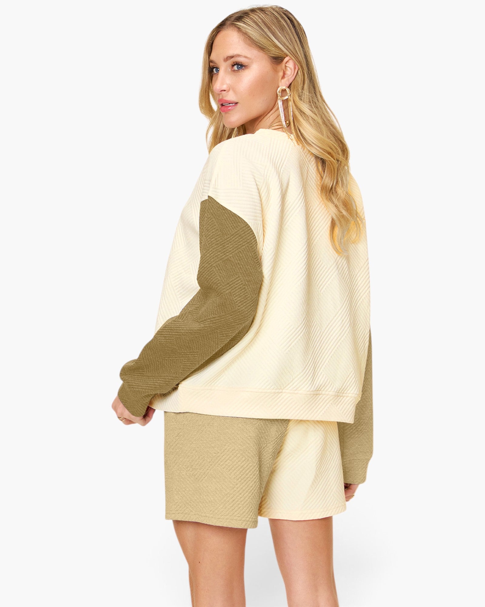 A woman modeling a cream and olive green color-blocked knit sweater and matching shorts against a light gray studio background.