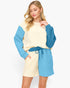 A woman modeling a color-blocked waffle-knit sweatshirt and shorts set. The set features a cream-colored body with bright blue sleeves and shorts, and a matching blue drawstring belt.