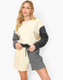 A woman modeling a color-block knit jumpsuit with a cream body, dark gray sleeves, and matching dark gray shorts with a drawstring waist, set against a plain light gray studio background.