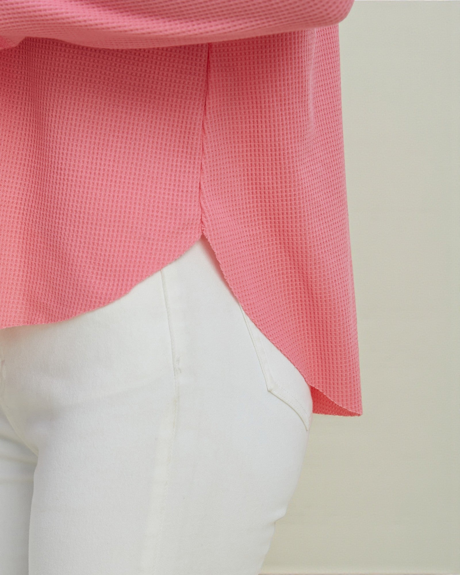 Close-up of a pink textured top and white pants on a neutral background