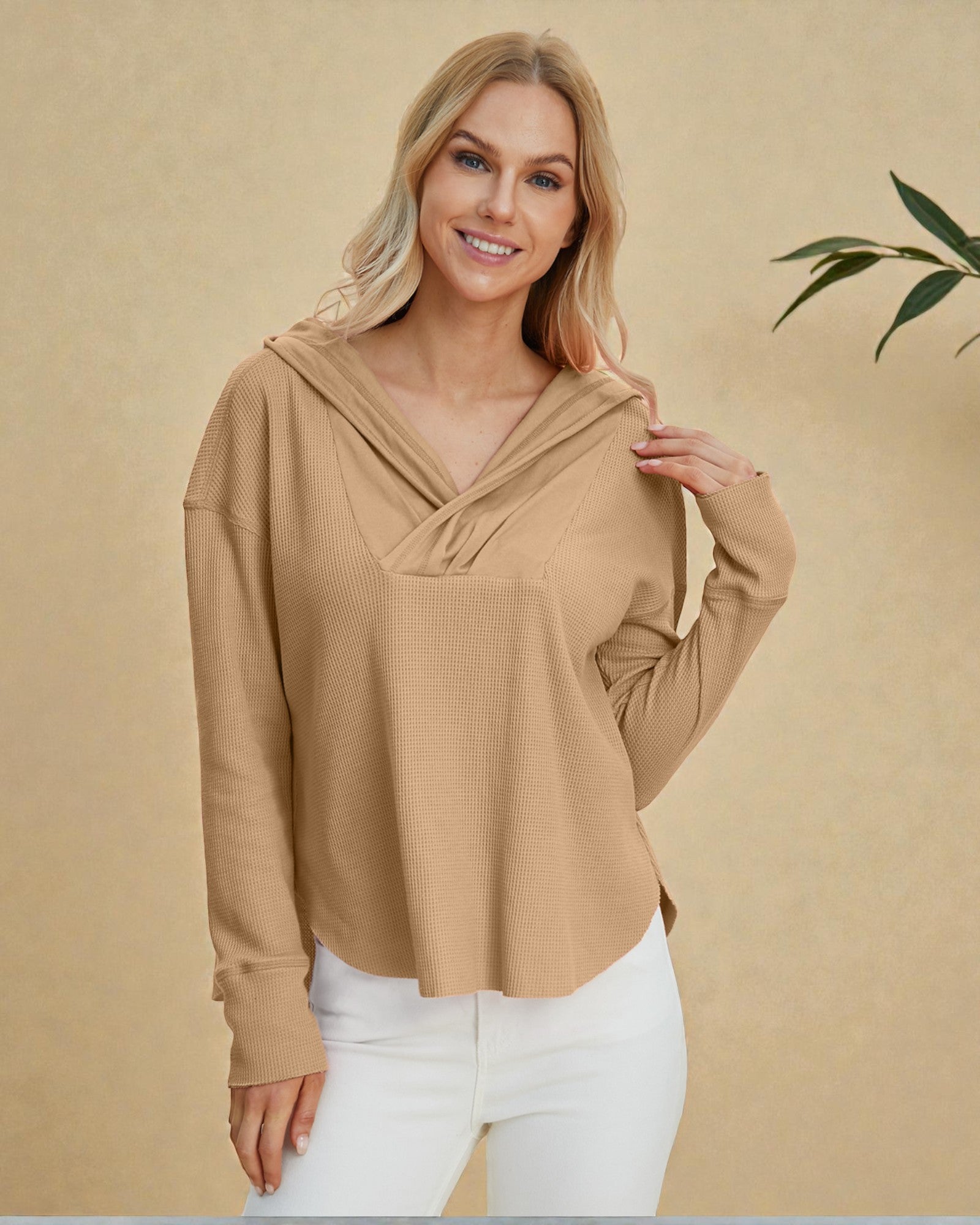 Woman wearing a beige long-sleeve top with a hood against a beige background