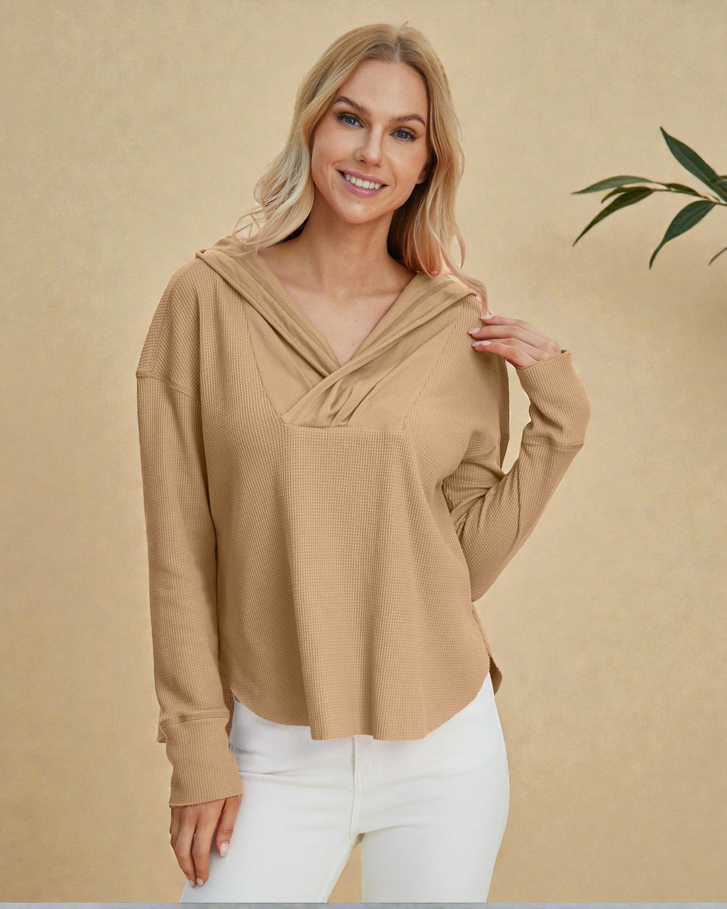 Woman wearing a beige long-sleeve top with a hood against a beige background