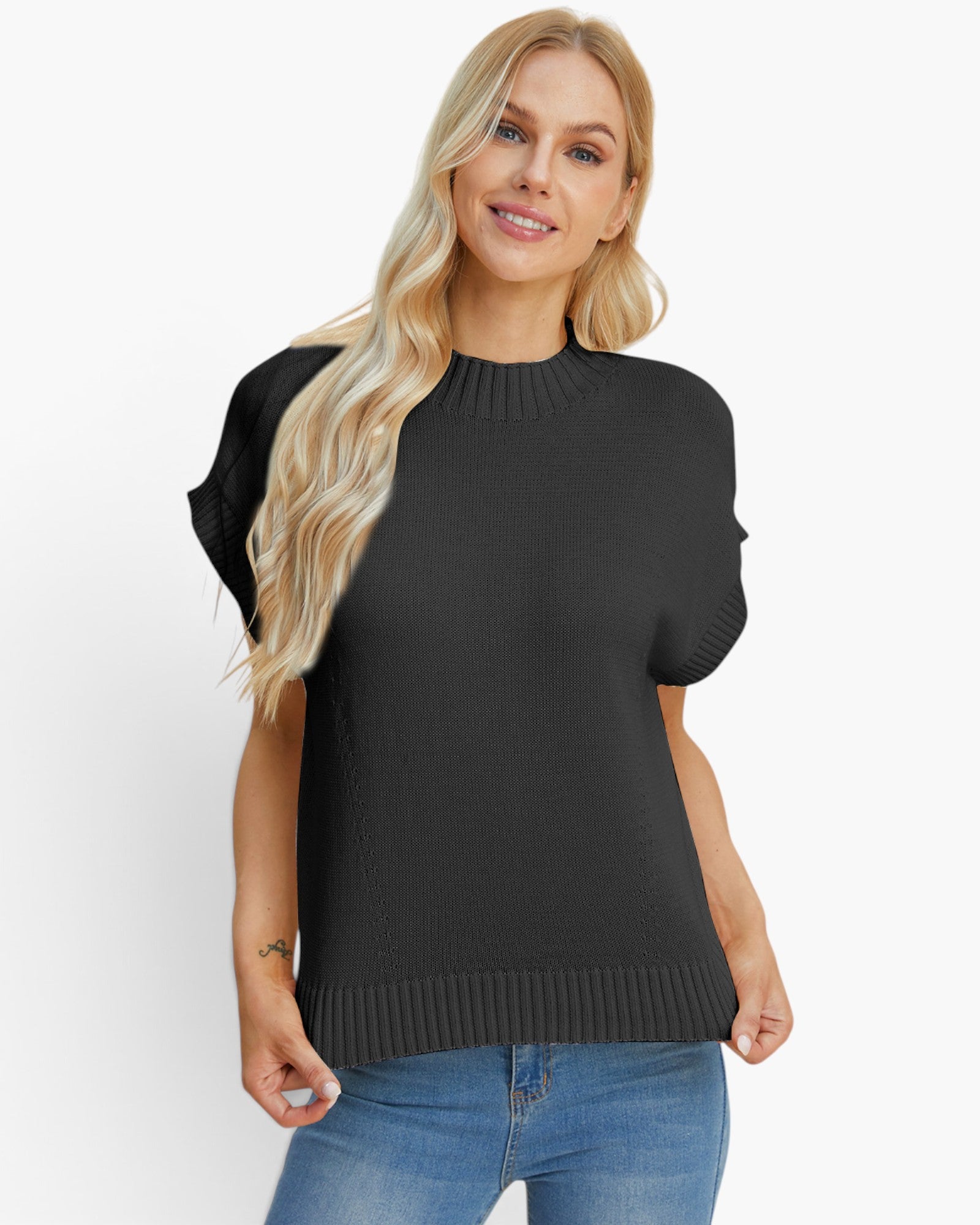 A blonde woman wearing a black short-sleeve mock-neck knit sweater and blue jeans, standing against a plain white studio background.