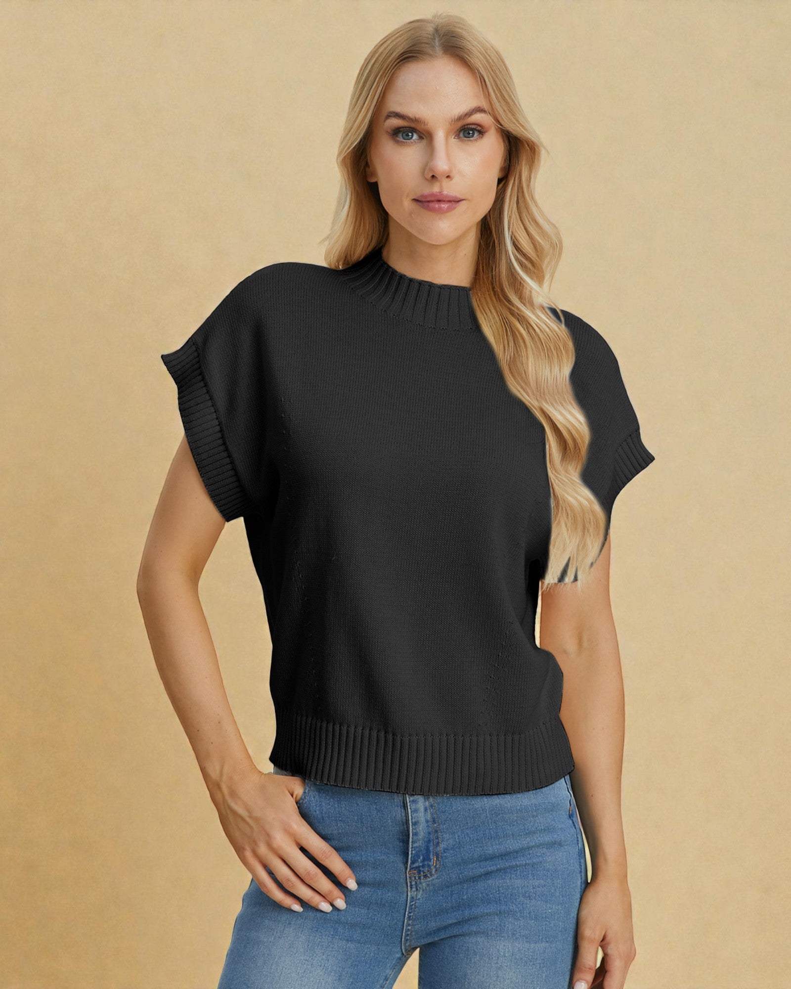 Woman wearing a black short-sleeve sweater and blue jeans against a beige background