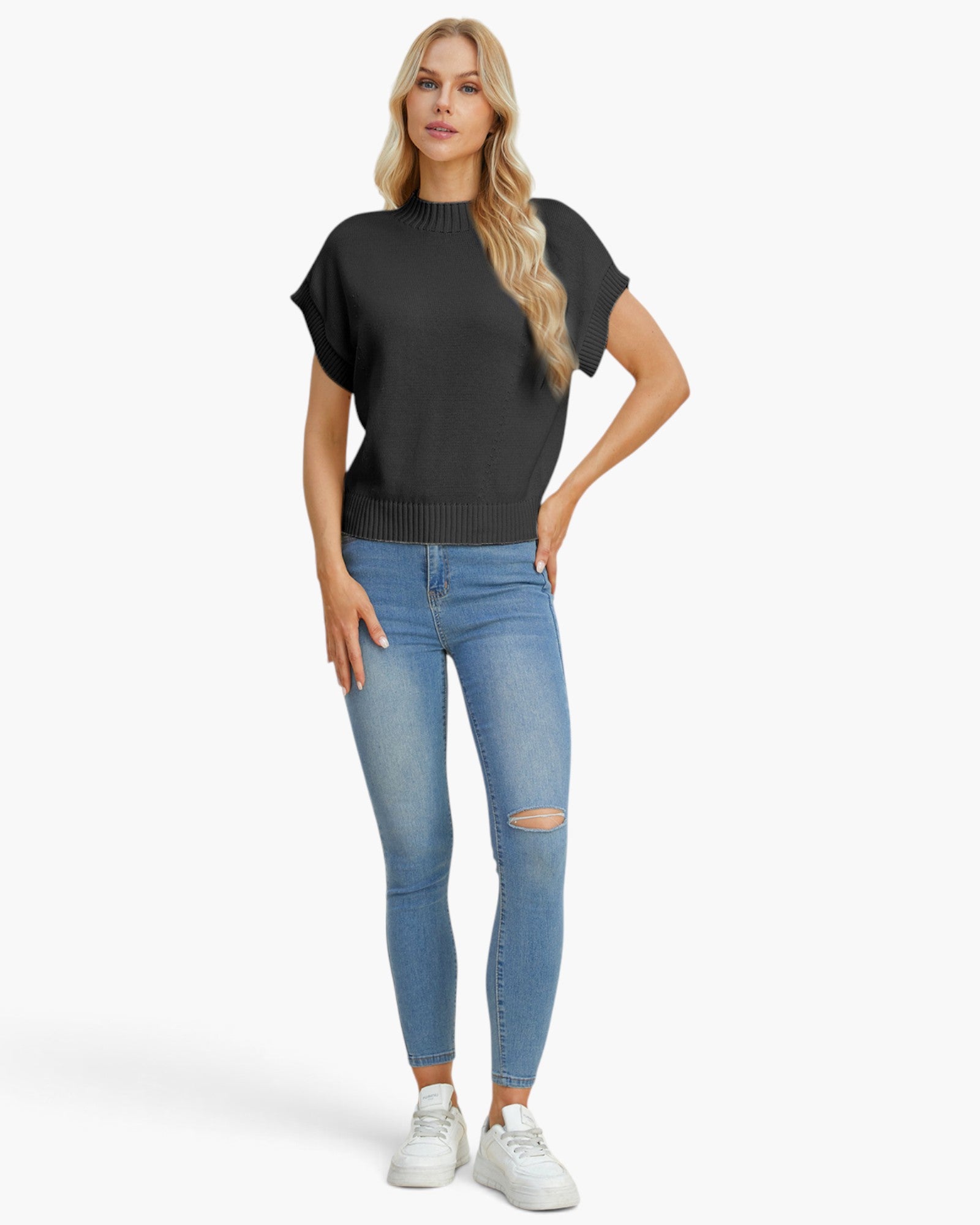 A woman modeling a black short-sleeve knit top with ribbed trim, paired with light blue distressed skinny jeans and white sneakers, against a plain white studio background.
