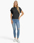 A woman modeling a black short-sleeve knit top with ribbed trim, paired with light blue distressed skinny jeans and white sneakers, against a plain white studio background.