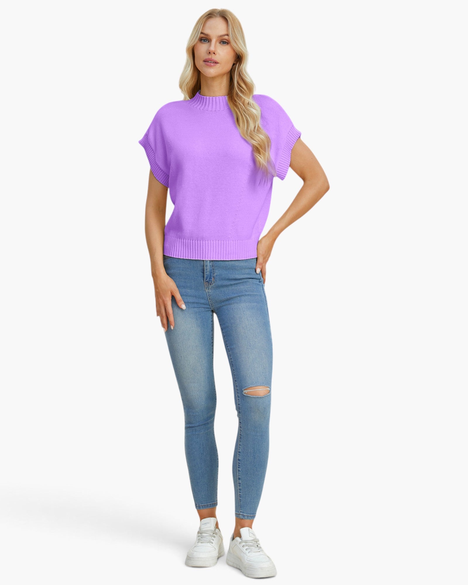 A woman modeling a light purple short-sleeve knit sweater with flared sleeves, paired with light blue ripped skinny jeans and white sneakers, against a plain white studio background.