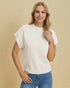 Woman wearing a white sleeveless sweater and blue jeans against a beige background