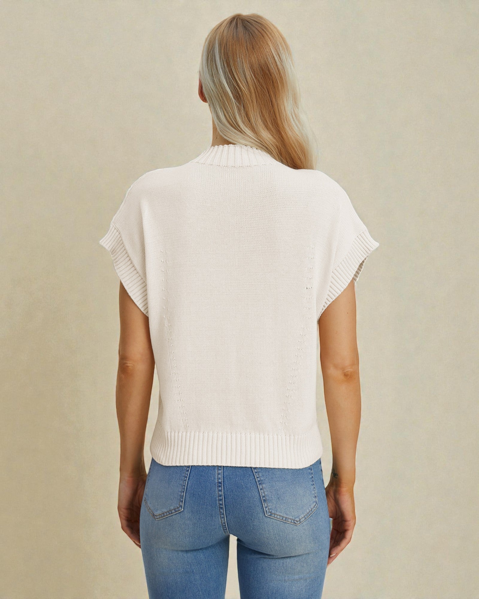 Person wearing a white sleeveless sweater and blue jeans on a beige background