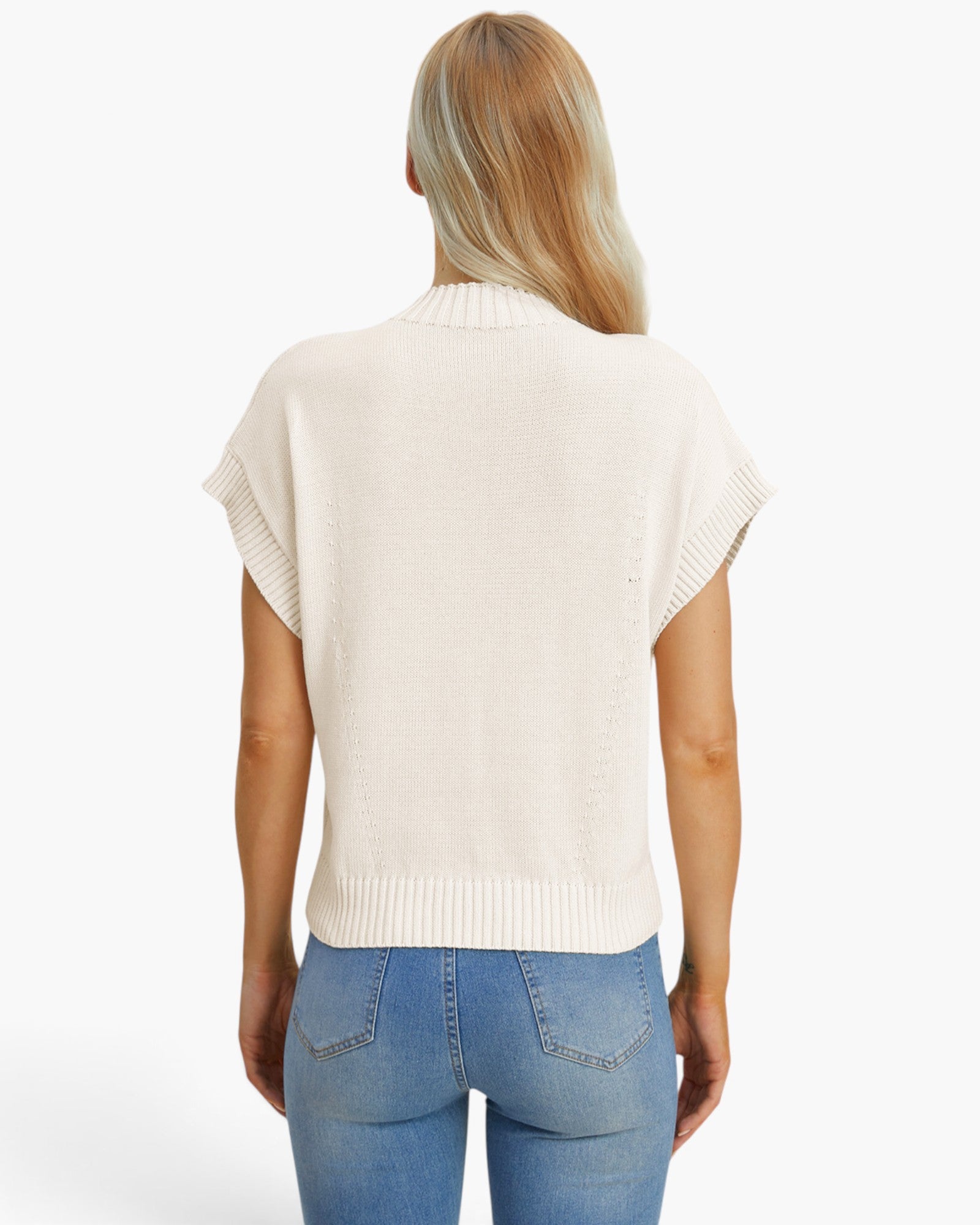 A woman viewed from the back wearing a cream-colored short-sleeve knit top and blue jeans against a plain white background.