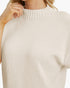 Close-up of a person wearing a cream-colored knit sweater with a ribbed mock neck and short sleeves, against a plain light background.