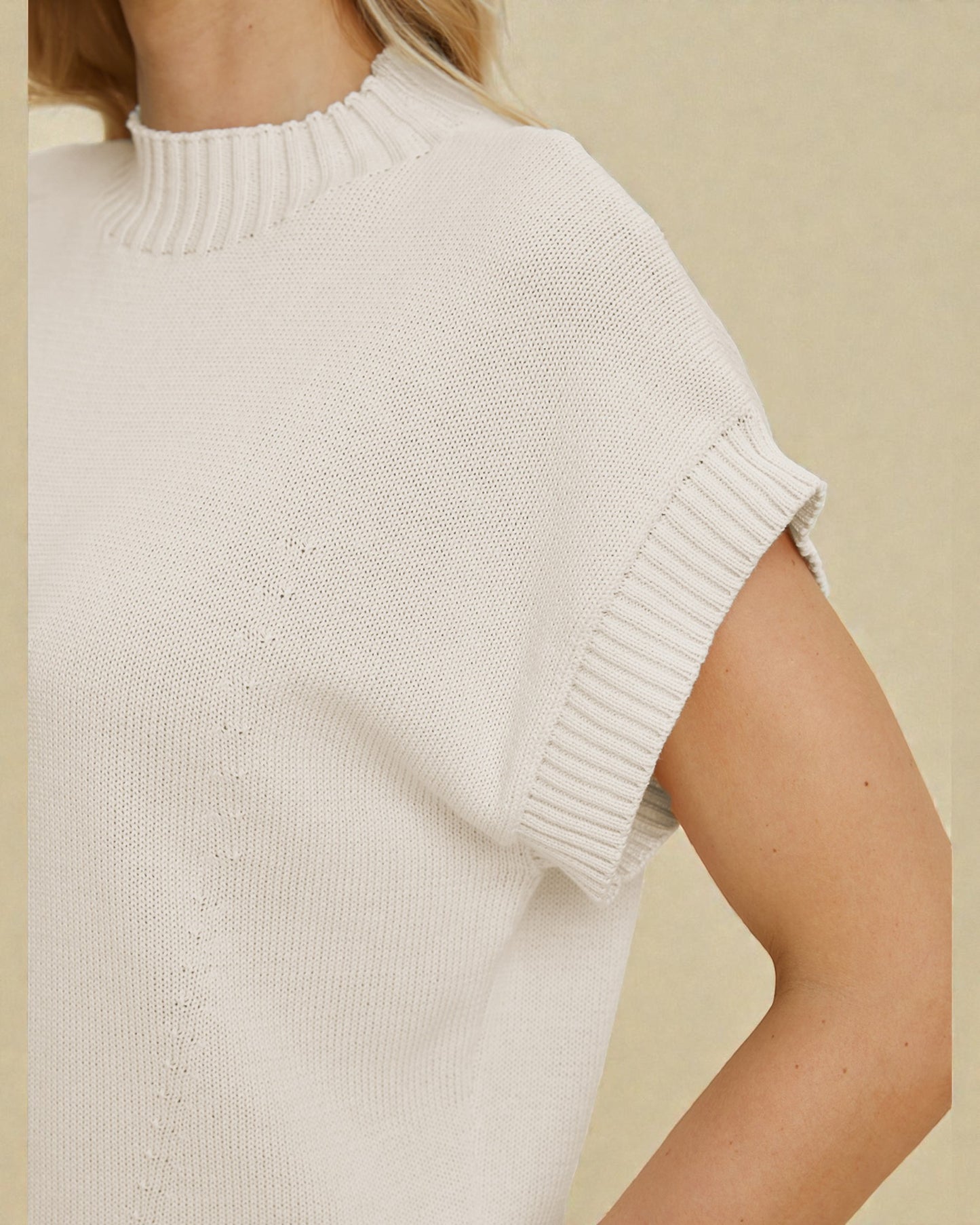 White knitted vest worn by a person on a beige background
