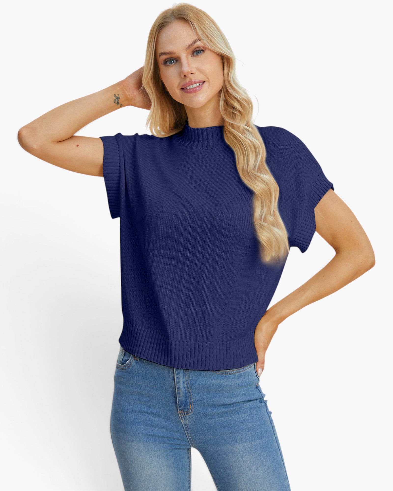 A blonde woman wearing a navy blue short-sleeve knit sweater and blue jeans, posing against a light gray studio background.