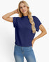 A blonde woman wearing a navy blue short-sleeve knit sweater and blue jeans, posing against a light gray studio background.