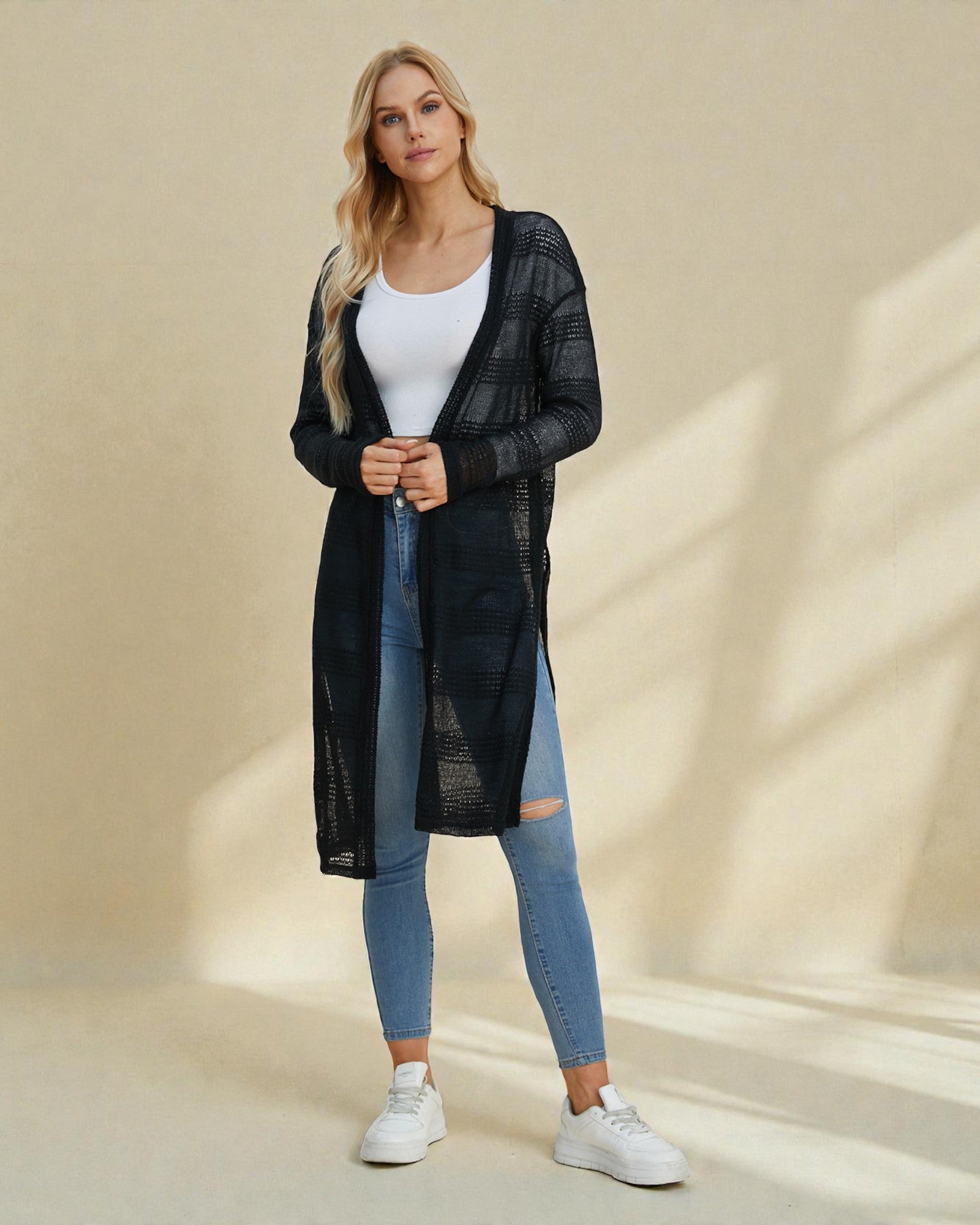 Woman wearing a black long-sleeve top, white t-shirt, blue jeans, and white sneakers on a beige background