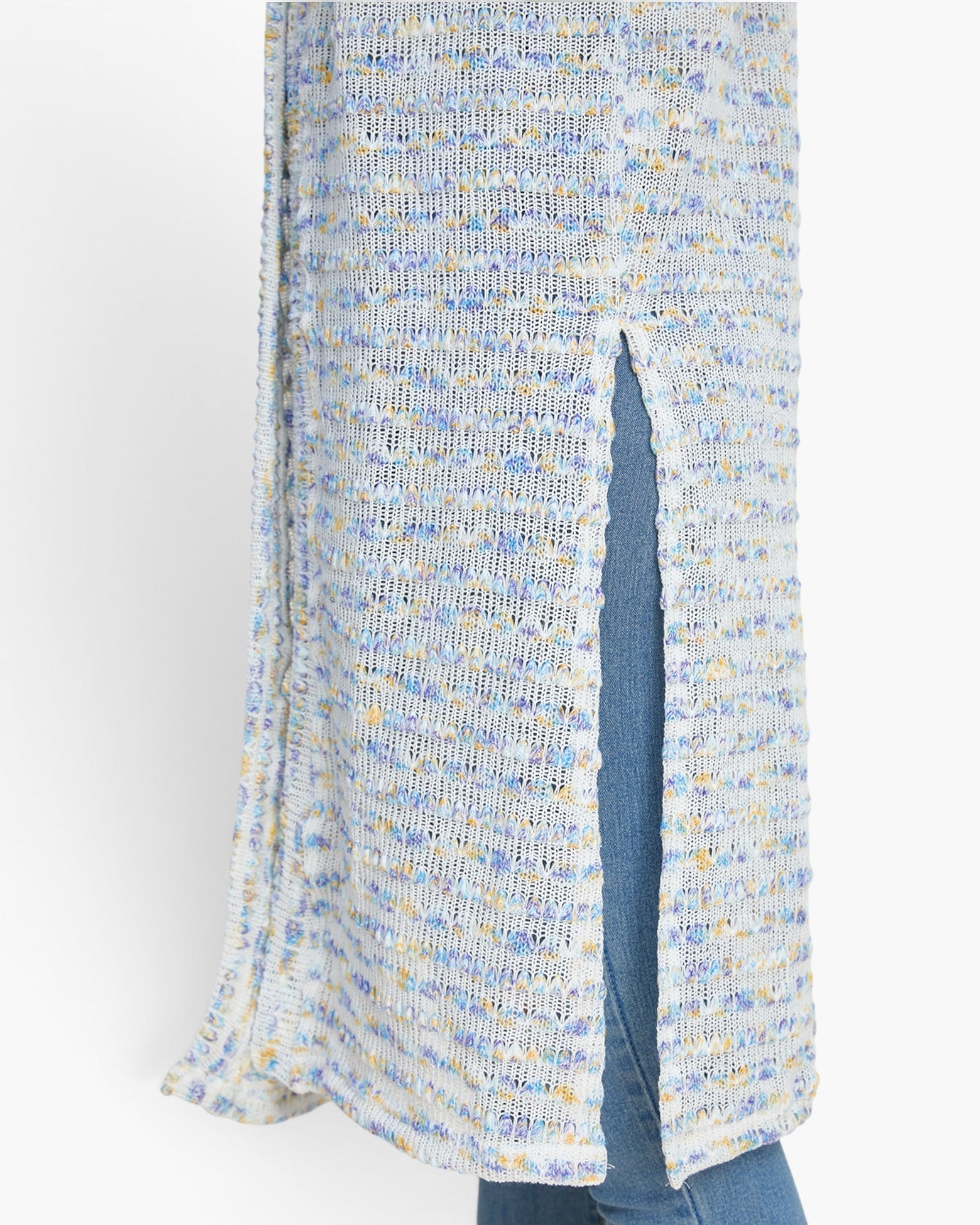 Close-up of a textured knit cardigan with a vertical front slit, featuring a marled pattern of light blue, white, and yellow, worn over blue jeans.